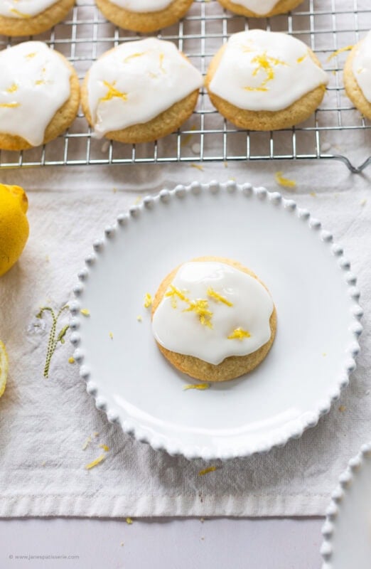 Lemon drizzle cookies with icing and lemon zest on a white plate.