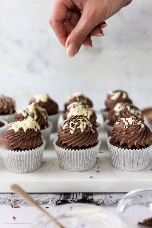 Sprinkling chocolate onto chocolate cupcakes
