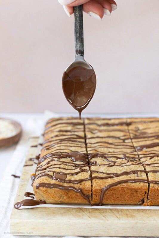 A spoon drizzling chocolate on Coconut Chocolate Blondies