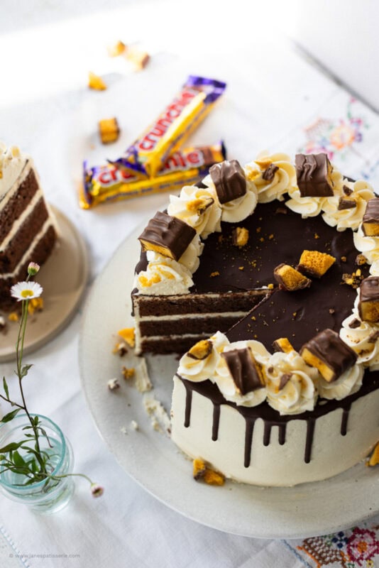 A slice missing of a crunchie drip cake with crunchies