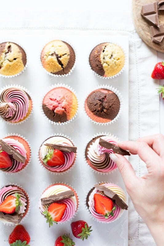 A hand decorating a Neapolitan Cupcake