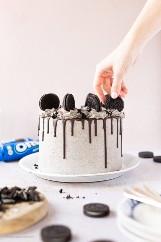 A hand placing an Oreo on an Oreo Drip Cake
