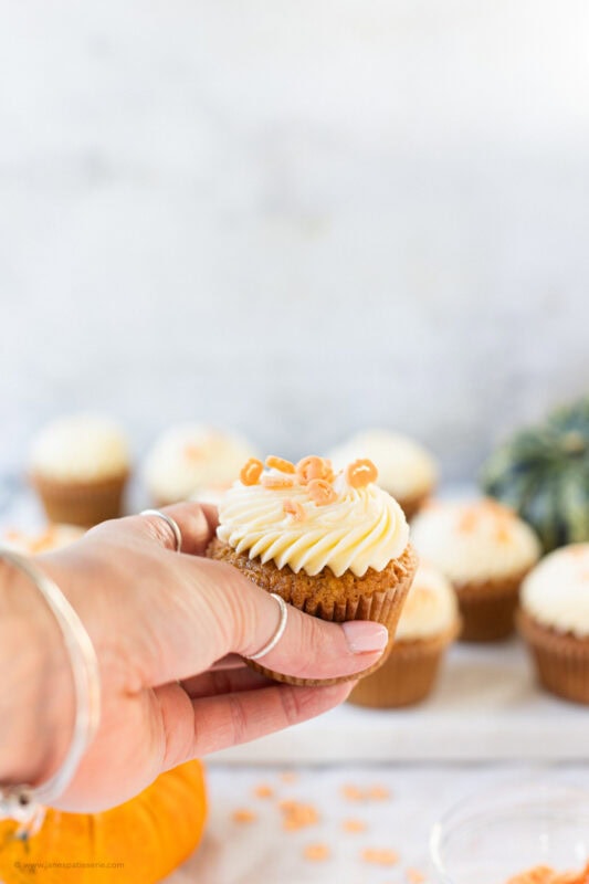 A hand holding a single Pumpkin Cupcake