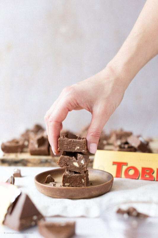 A hand taking a square of Toberlone Fudge from the plate