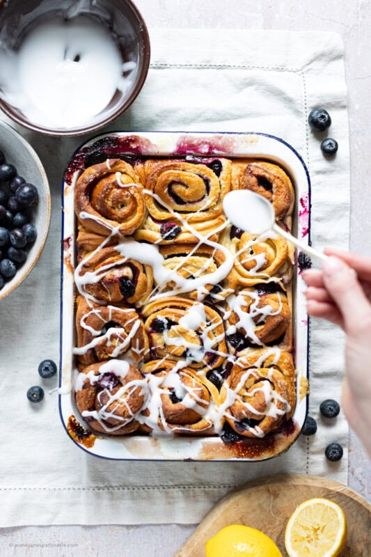 A spoon drizzling icing on lemon and blueberry rolls