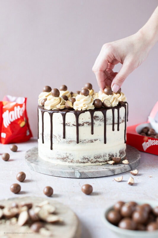 A hand placing the final decorations on a Malteser Drip Cake
