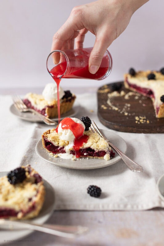 Pouring coulis on a slice of Apple and Blackberry Crumble Pie