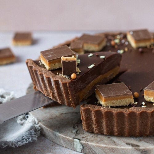 A slice being taken from a Billionaires Tart with Millionaires Shortbread in the background