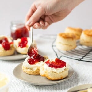 A hand spooning jam onto a buttered classic buttery scone