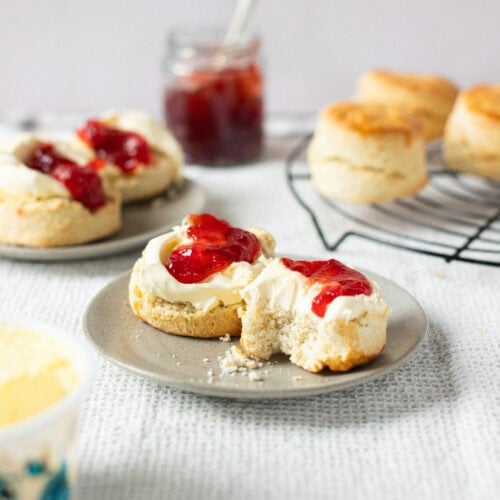 Two classic buttery scones on a plate with a bite taken from one