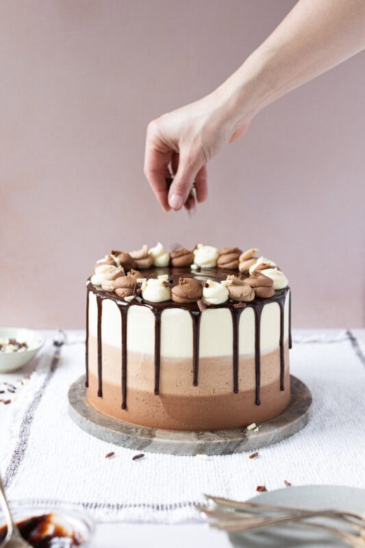A hand decorating a Triple Chocolate Cake