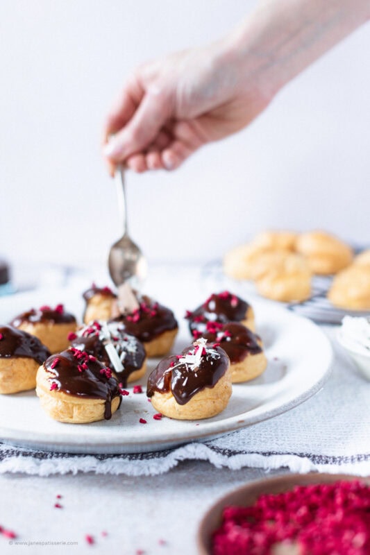 A hand decorating the final touches to a plate of profiteroles