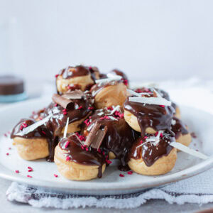 A plate of piled profiteroles covered in chocolate sauce