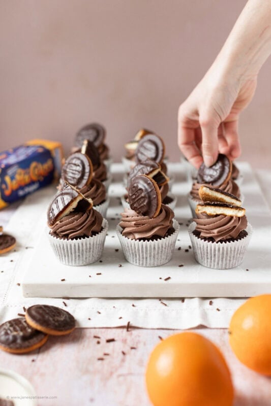 A hand decorating one of the Jaffa Cake Cupcakes
