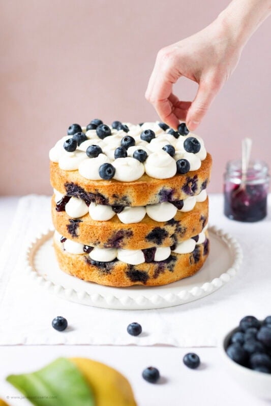 A hand decorating the final touches on a Lemon Blueberry Cake