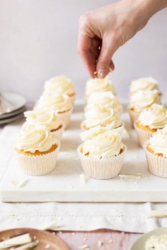 A hand decorating baked White Chocolate Cupcakes
