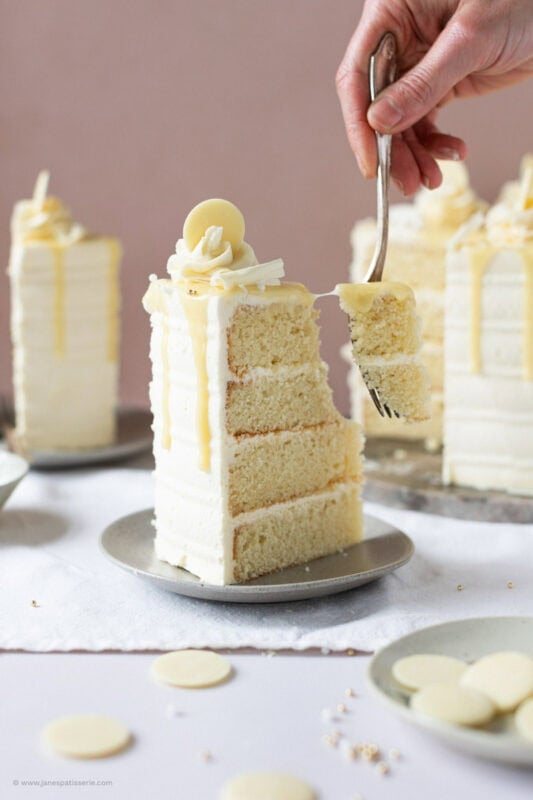 A fork taking a bite from a slice of White chocolate drip cake