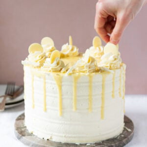 A hand placing the final decorations on a white chocolate drip cake