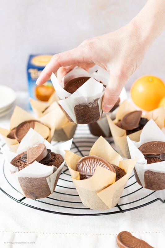 A hand taking a Chocolate Orange Muffin from a cooling rack