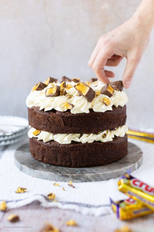 A hand decorating a Honeycomb Crunchie Cake