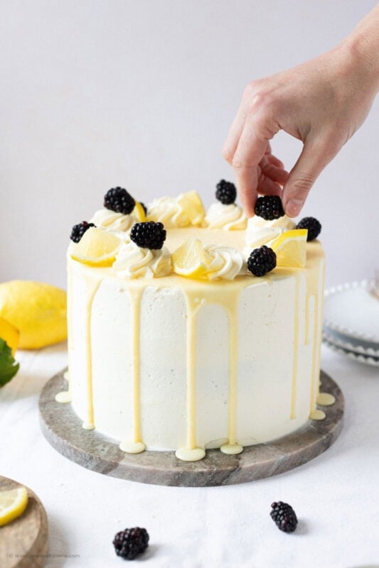 A hand decorating the final touches on a Lemon Elderflower Cake